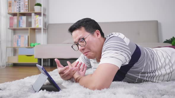 Asian man lying and taking video call on tablet in living room