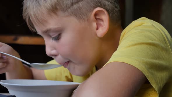 Closeup of a Teenage Boy in a Yellow Tshirt Eats Soup with a Spoon From a Bowl alt