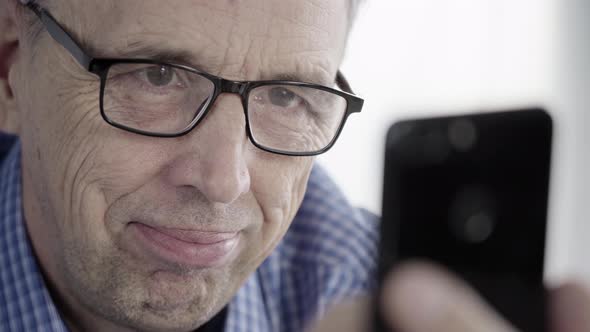Man With Glasses Looks at the Smartphone Screen and Smiles alt