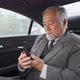 Stressed senior businessman sitting on car back seat using mobile phone talking to business partner