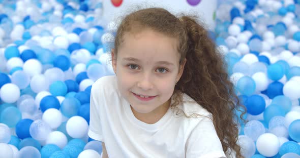 Portrait of a Cheerful Little Girl Smiling Child Jumps Out of Children's Plastic Ballskid Looks at alt