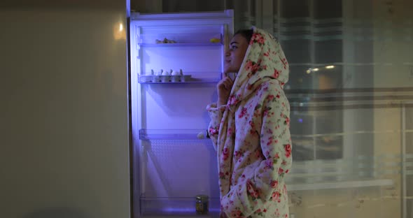 Young Woman Opens the Refrigerator at Night and Takes Food