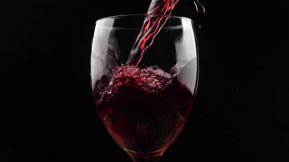 Wine. Red wine pouring in wine glass over dark background. Rose wine pouring from the bottle. Slow m