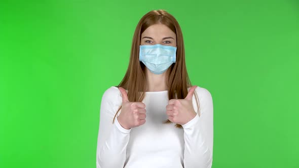 Portrait of Happy Pretty Young Girl in Medical Protective Face Mask Looking at Camera and Showing alt