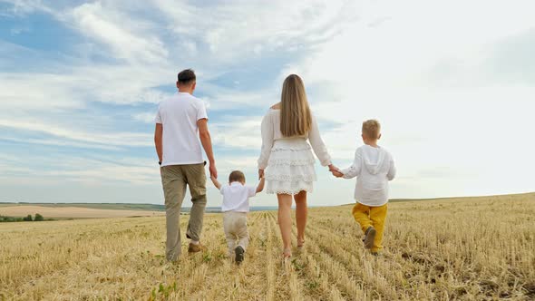 Family with Children Walks Joining Hands on Mown Wheat Field alt