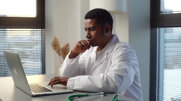 Happy AfricanAmerican Male Doctor Finishing Working on Laptop Computer and Having Coffee Break alt