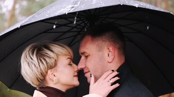 Man and Woman Standing Under Umbrella in Rain in Forest alt