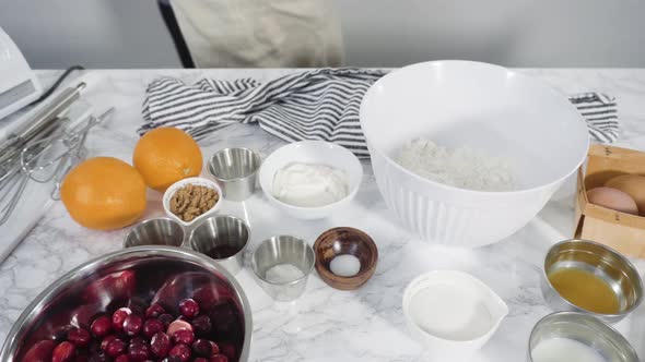 Step by step. Ingredients to bake cranberry muffins on a marble kitchen surface. alt