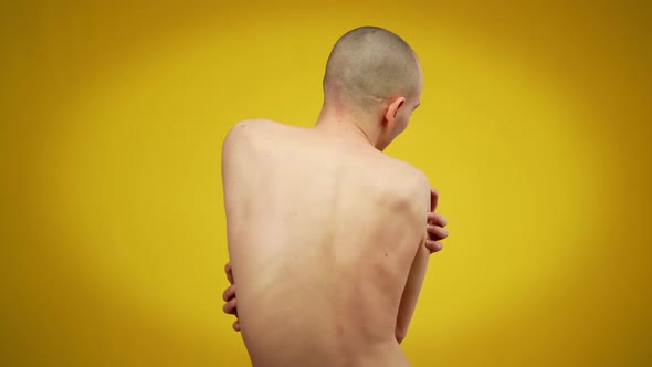 Back View of Young Man Hugging Himself Standing at Yellow Background alt
