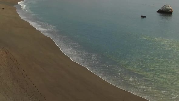 A drone flies toward small ocean waves crashing ashore. alt