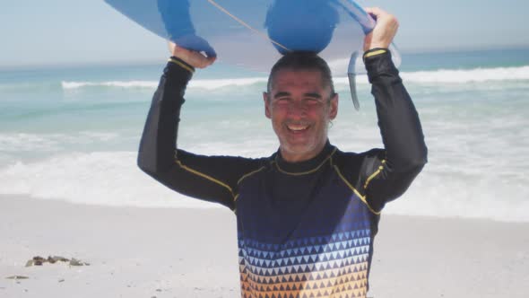 Senior Caucasian man holding a surfboard on the beach alt
