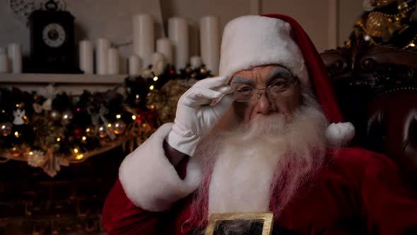 Close Up Santa Claus Looks Camera Sitting on Chair at Home Christmas Holidays alt