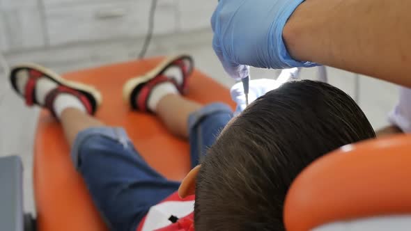 a Pediatric Dentist Grinds a Filling in the Mouth of a Teenage Patient Sitting in an Orange Dental