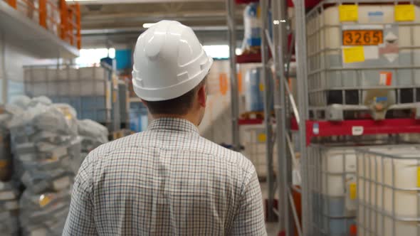 Back View of Male Manager in Helmet Walking in Industrial Warehouse alt