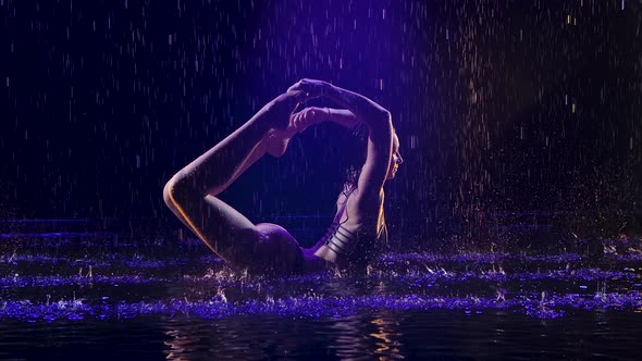 Bow Pose Performed By a Young Sportswoman in a Dark Studio in the Rain. Studio Light Creates Shimmer alt