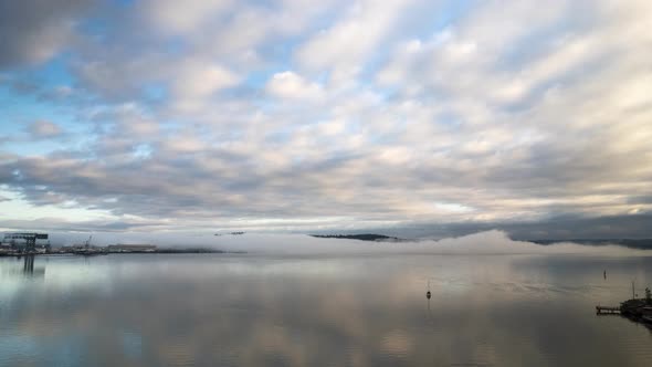 Fog billows across still water as marine layer clouds stream across the sky, aerial hyperlapse alt