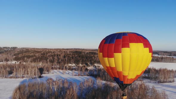 Aerial Shot of the People Fly on a Big Bright Balloon Over the Winter Forest