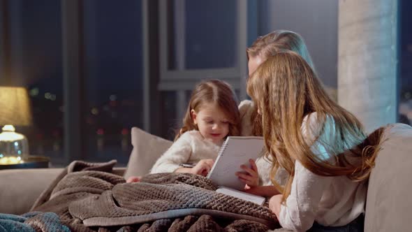 Caring Mother Spending Evening Time with Daughters on Sofa alt