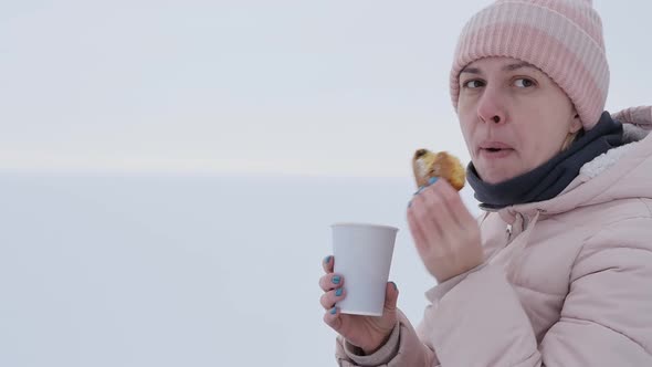 Portrait Young Woman on the Shore of the Frozen Sea Eats a Bun and Drinks Coffee