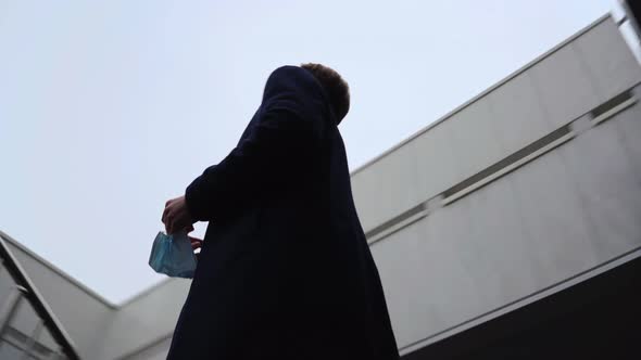Sad Young Man Taking Medical Mask Off His Face Under Snowfall alt