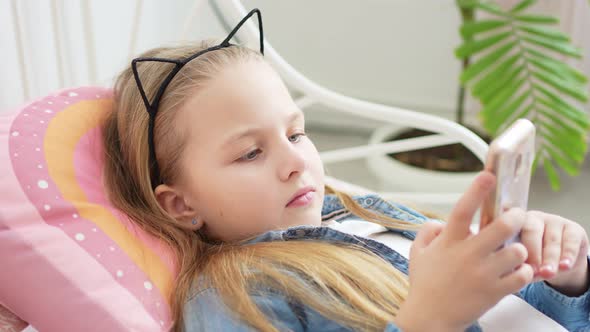 a Beautiful Little Girl in a Rim with Cat Ears with a Phone in Bed alt