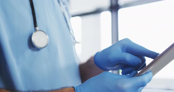 Caucasian male doctor wearing protective gloves using digital tablet alt
