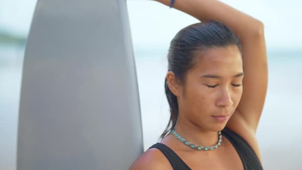 4K Portrait of Asian woman in swimwear holding surfboard walking on tropical beach at summer sunset. alt