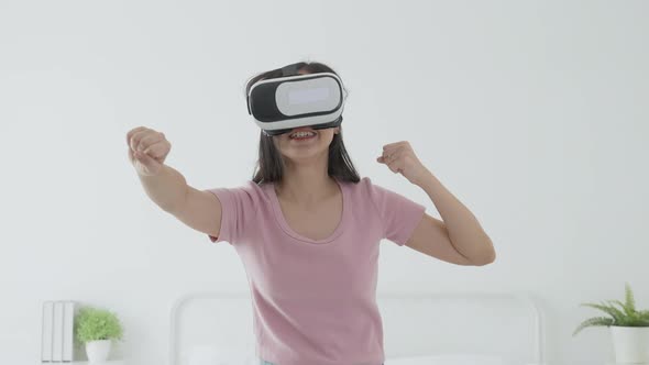 Young asian woman wearing vr headset playing game with excited on bed in the bedroom at home. alt