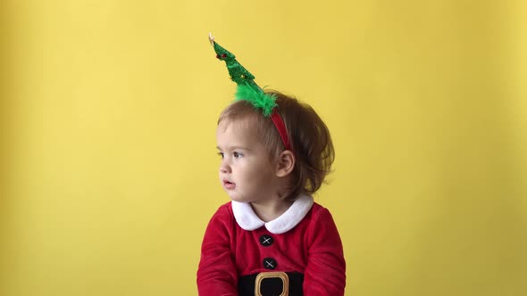 Portrait Emotion Happy Chubby Toddler Baby Girl In Santa Suit Raises Hands Up With Christmas Tree on