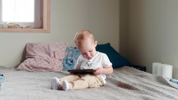 Baby Boy Sitting on Bed and Playing on Tablet