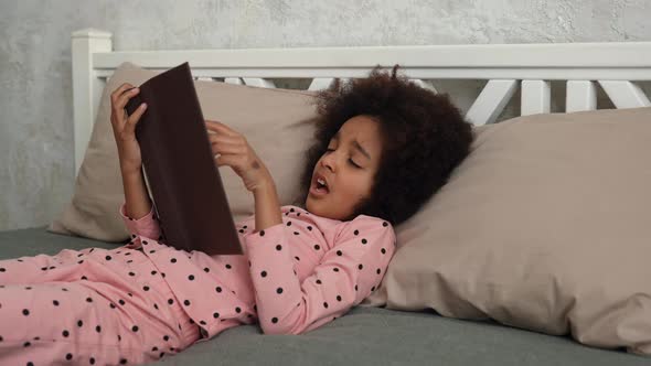 Cute Little African American Girl Reads a Book with Fairy Tales and Falls Asleep alt