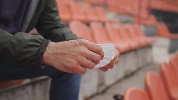 Closeup of a Medical Mask in the Hands of a Man Sitting Alone in a Sports Stadium