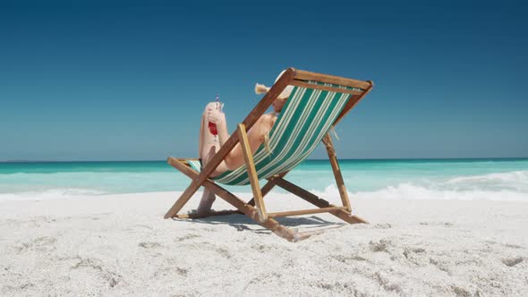 Woman drinking cocktail on deck chair on the beach alt