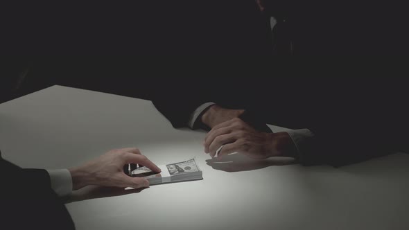 Businessman giving bribe money to his partner in dark room