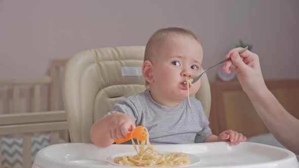 Mom feeds a newborn baby aged 12-17 months spaghetti with tomato sauce. Toddler eats pasta alt