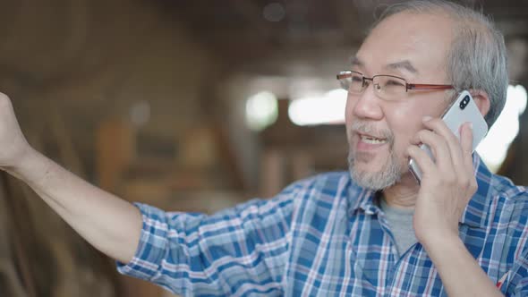 Asian senior carpenter talking on the phone with customer alt