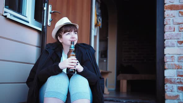 Cinematic Shot of Cowboy Woman Drinking Beer on the Porch of the House Woman Relaxes Near the House