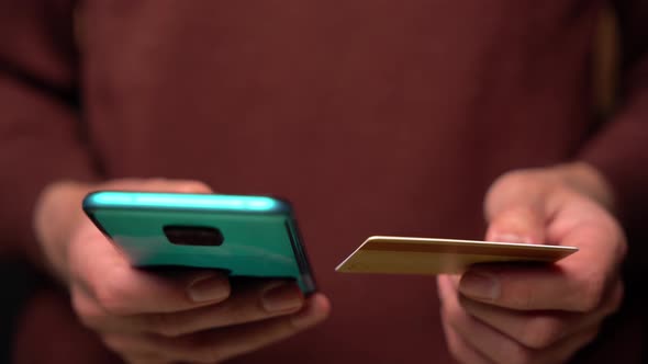 Close-up of a man in a beige sweatshirt holding a smartphone and a credit card in his hand