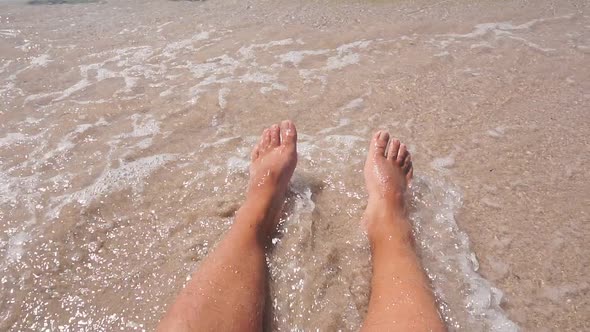 Closeup of a Man's Feet on the Sand in the Azure Sea Water Small Waves Beating Against His Legs