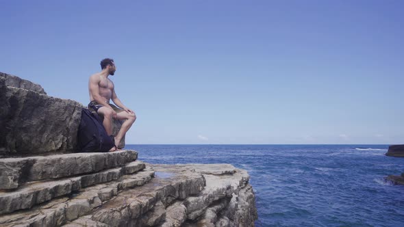 Man sitting on cliffs by the sea. alt