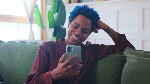 Young Positive African American Woman Making Video Call Via Phone Sits on Couch alt
