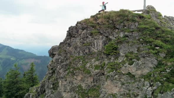 Aerial View of Woman Stands on Mountain Peak with Raised Arms Enjoying Success