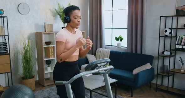 Woman in Training Clothes Running on Treadmill and Simultaneously Listening Favourite Music alt