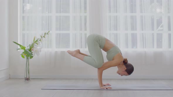 Side view of Asian woman wearing green sportwear doing Yoga exercise in front of windows alt