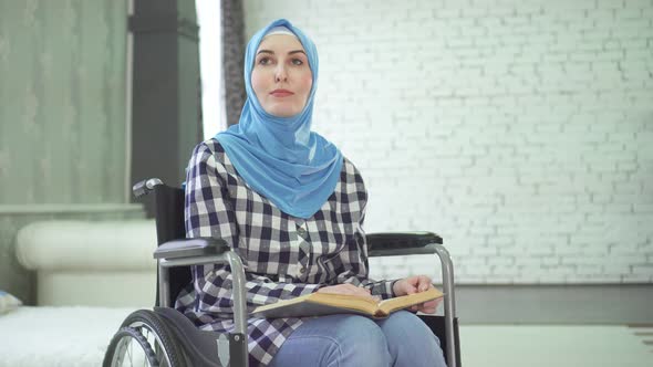 A Beautiful Young Woman in a Hijab Is Blind or Weakly Imposing a Wheelchair Reading a Braille Font alt