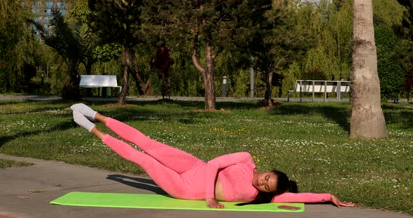 Young woman stretches her leg sitting on a yoga mat in the park.