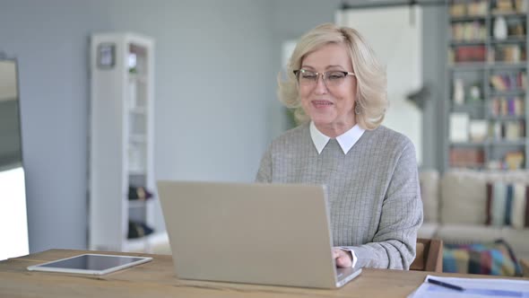 Old Woman Doing Video Chat on Laptop in Modern Office alt