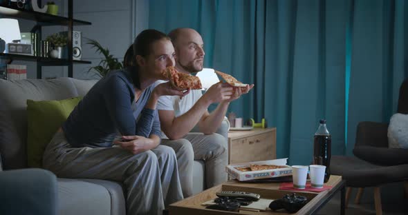Happy couple sitting on the couch and eating pizza