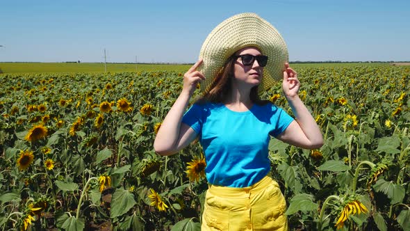 Adorable young girl in a straw hat, yellow skirt and blue t-shirt smiling in sunflowers field alt