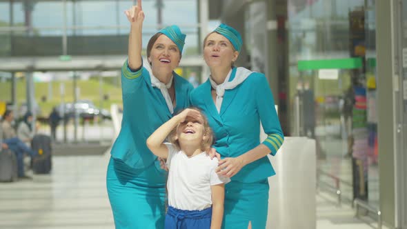 Charming Little Girl Standing with Stewardesses Next To Airport and Looking at Plane Takeoff alt